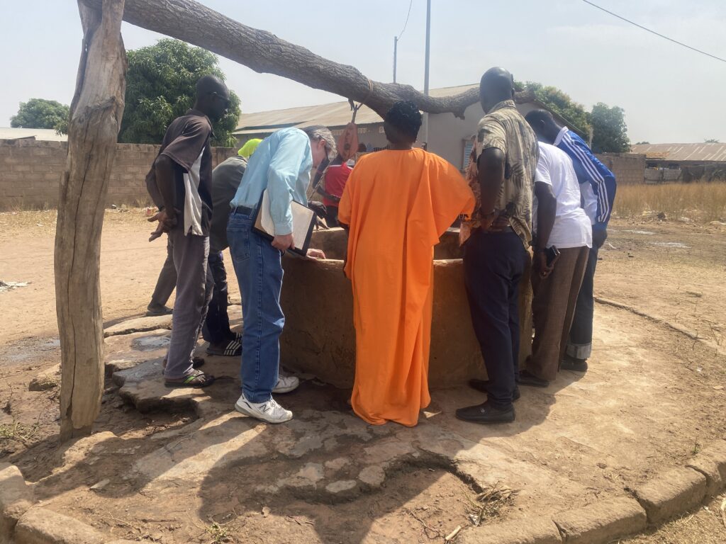 A group of people look inside a well in a dry, dusty landscape.