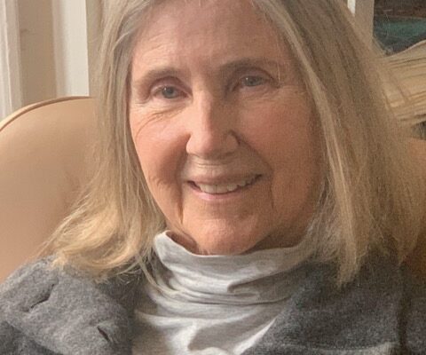 Shoulder length gray hair, gray turtleneck, sweater, warm smile