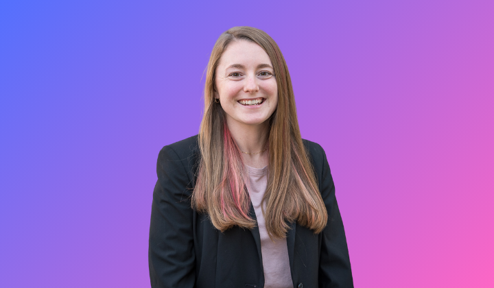 A young white woman with long, pink-streaked brown hair, wearing a black suit jacket and smiling widely