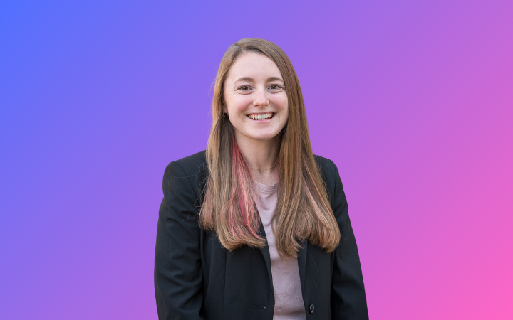 A young white woman with long, pink-streaked brown hair, wearing a black suit jacket and smiling widely