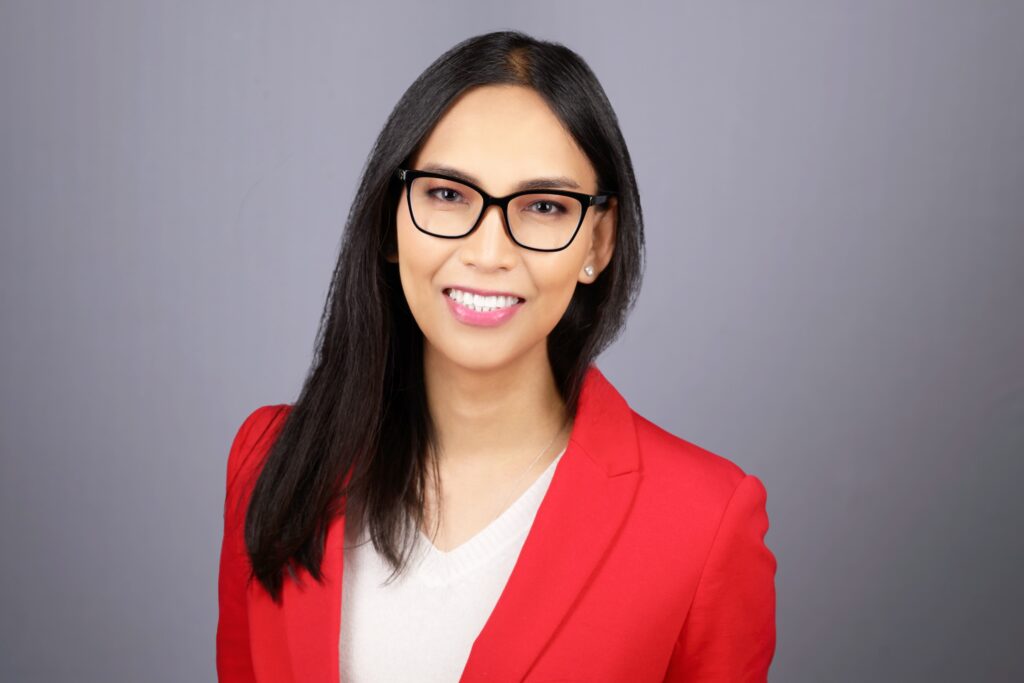 Margaret Gamalo has long dark hair, glasses, and a red suit jacket.