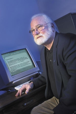 A photo of Karl Peace with a white beard and a dark suit jacket sitting in front of a now-vintage desktop computer.