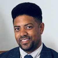 Kory Trott has short black hair and is wearing a navy blue suit jacket.
