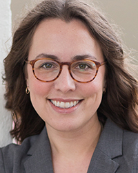 A white woman with wavy brown hair and brown glasses smiles