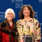 Donna Brogan (white hair and glasses in a red shirt) presents a plaque to Donna Spiegelman (curly brown hair, yellow patterned shirt) with a plaque in front of an Emory University Rollins School of Public Health background.