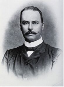 A black and white photo from the early 20th century of a man with short hair and a mustache