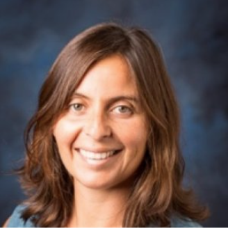 Anna Bargagliotti smiles at the camera. She had shoulder-length, wavy, brown hair and is wearing a blue top.