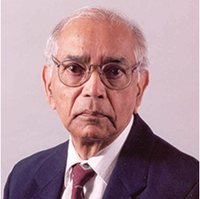 C.R. Rao wears a navy jacket, red tie, white shirt, and round glasses. He has short white hair.