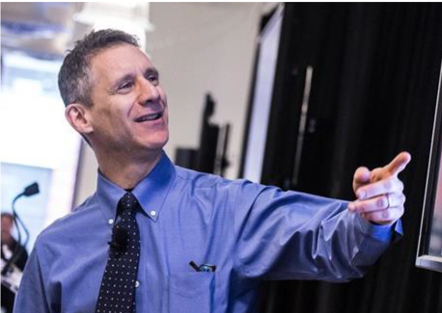 Andrew Gelman points at a screen. He is wearing a blue dress shirt, a navy patterned tie, and he has short, dark gray hair.