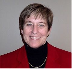 Linda Young wears a red jacked, black turtleneck shirt, and a pixie haircut.