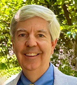 Stephen Provasnik has white hair and is wearing a blue shirt with a blue and white striped jacket.