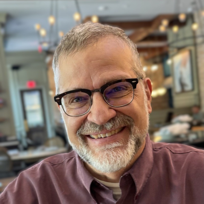 Steve Pierson wears a maroon collared shirt, glasses, and has short gray hair and a short beard.