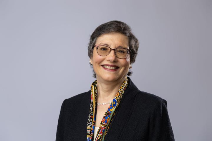 Erica L. Groshen wears a pixie haircut, glasses, a dark jacket, and a colorful patterned scarf.
